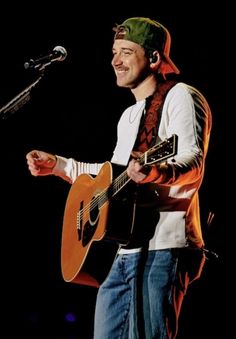 a man holding a guitar while standing next to a microphone and wearing a green bandana