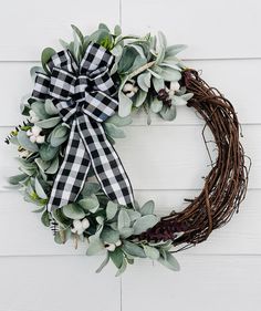 a wreath is hanging on the side of a white wall with greenery and flowers