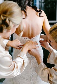 two women helping another woman put on her wedding dress