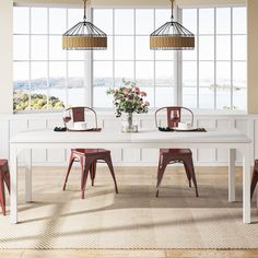 a dining room table with four chairs in front of large windows and a vase filled with flowers