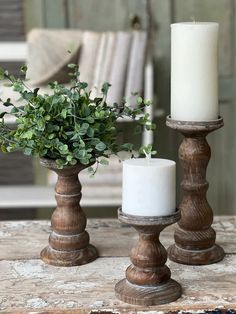 two candles are sitting next to each other on a table with greenery in them