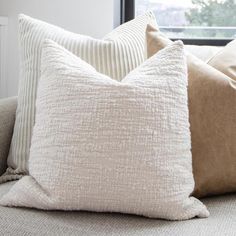 three pillows sitting on top of a couch next to a window