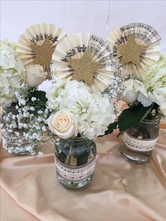 three vases filled with white flowers on top of a cloth covered tablecloth,