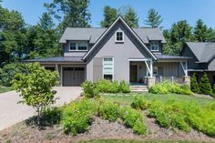 a house in the woods with lots of trees and bushes on the front lawn, surrounded by greenery