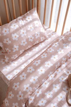 a crib bed with pink and white flowers on it, next to a stuffed animal