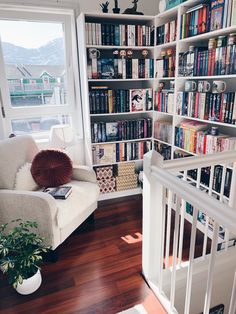 a white chair sitting in front of a book shelf filled with books next to a window