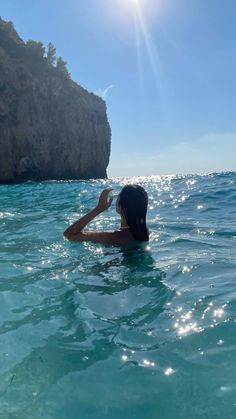 a woman swimming in the ocean next to a cliff