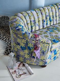 a blue and yellow flowered couch sitting on top of a white floor next to a vase