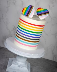 a multicolored striped cake with two heart shaped buttons on it's top