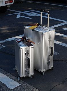 two silver suitcases sitting on top of a parking lot next to a white van