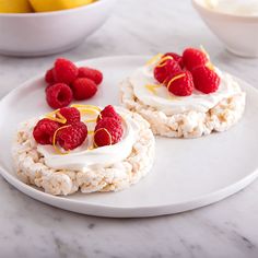 two desserts with raspberries and whipped cream are on a plate next to lemons