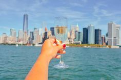 a person holding up a wine glass in front of a cityscape on the water