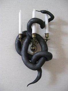 a wall mounted candle holder with two candles in the shape of a snake's head