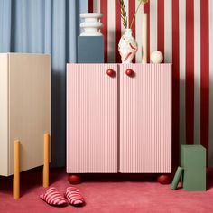 a pink cabinet sitting in the middle of a room with red and white striped walls