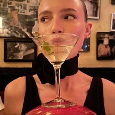 a woman wearing a black bow tie holding a martini glass in front of her face