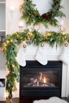 stockings hung over a fireplace with christmas lights and greenery on the mantel above it