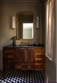 a bathroom with black and white checkered flooring, gold framed mirror and wooden vanity