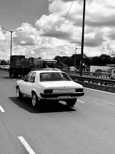 a white car driving down a street next to a train on the tracks in black and white