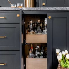 an open cabinet in a kitchen filled with liquor bottles and flowers on the counter top