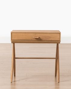 a wooden desk with two drawers sitting on top of wood flooring next to a white wall