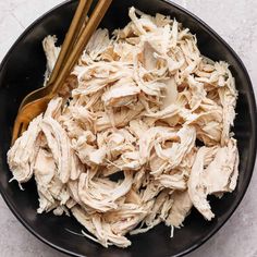 a black bowl filled with shredded chicken and two wooden spoons