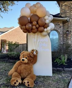 a brown teddy bear sitting next to a bunch of balloons on top of a sign