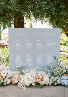 an outdoor seating arrangement with flowers and greenery on the side of a large sign