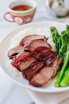 a white plate topped with meat and veggies next to a cup of tea