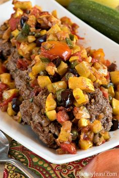 a white plate topped with meat and veggies next to a zucchini