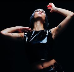 a woman with her hands behind her head in the air, wearing black latex