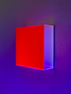 a red and purple light shines on the wall above a square shaped object that appears to be rectangleed