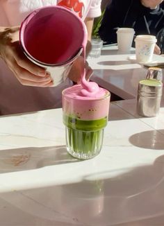 a person pouring pink and green liquid into a cup