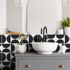 a bathroom sink sitting under a mirror next to a potted plant on top of a dresser