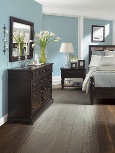 a bedroom with blue walls and wooden floors, white flowers on the nightstands and a large bed