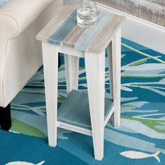 a small table with a glass on it in front of a couch and blue rug