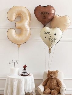 three balloons shaped like numbers and two teddy bears sitting on chairs in front of a table