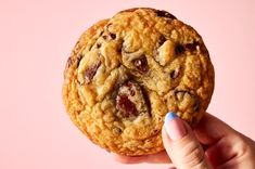 a close up of a person holding a chocolate chip cookie in front of a pink background