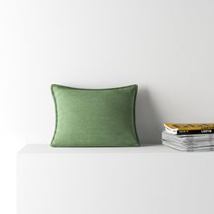 a green pillow sitting on top of a white shelf next to a stack of books