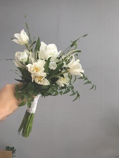 a bouquet of white flowers being held by a person's hand in front of a gray background