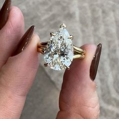 a woman's hand holding an engagement ring with a pear shaped diamond in it