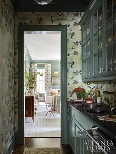 an open door leading to a kitchen with green cabinets and wallpaper on the walls