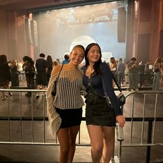 two women standing next to each other in front of a stage with people on it