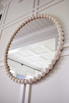 a round mirror hanging on the wall next to a white door with a wooden beaded frame