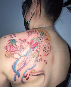 a woman's back with colorful tattoos on her upper half and the top part of her shoulder