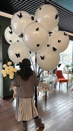 a woman standing in front of balloons that are shaped like bats and butterflies on the ceiling