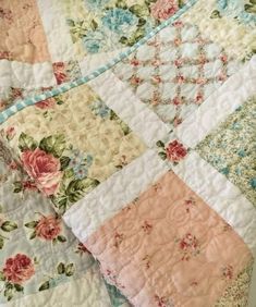 an old quilt is laying on top of a bed with pink and blue flowers all over it