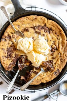 a skillet with ice cream and chocolate chip cookie in it next to spoons