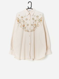 Vintage embroidered appliqué blouse with pretty floral design. This pretty beige blouse has golden brown and multicoloured flowers embroidered onto the front to create a truly beautiful piece! This blouse also features a full length button closure and buttoned cuffs. Made from a lightweight soft cotton.  Our recommended size: Large Label says: No size label Condition: Very good Material: 100% cotton Measurements in inches: Pit to pit: 23.5 Shoulders: 20.5 Front length: 30 Back length: 30.5 Sleeve length:23 Hem: 23 We recommend that you compare our measurements to a similar item of your own to ensure good fit. Measurements are taken flat and doubled for waist and hip. Our items are vintage and may show signs of previous wear, etc. Any significant wear, damage or obvious marks will be photog Elegant Long Sleeve Blouse With Floral Applique, Cotton Button-up Blouse With Floral Embroidery, White Long Sleeve Blouse With Floral Applique, Spring Beige Button-up Blouse, Feminine Embroidered Beige Tops, Beige Floral Print Button-up Blouse, Feminine Cotton Blouse With Floral Embroidery, Beige Button-up Blouse With Floral Print, Feminine Long Sleeve Embroidered Tops