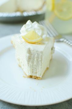 a slice of lemon pie on a plate with a fork and glass in the background