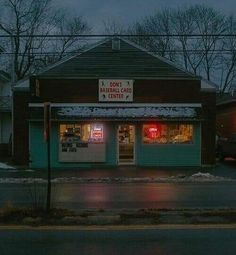 an empty street in front of a store at night with snow on the ground and cars parked outside